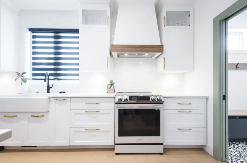 Cuisinière encadrée par des armoires blanches, hotte cheminée en inox et dosseret en céramique – design d’intérieur élégant signé Catherine Paradis.