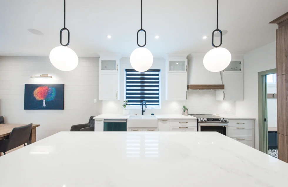 Cuisine à aire ouverte avec armoires blanches, grand îlot central et suspensions contemporaines – design fonctionnel et épuré de Catherine Paradis.